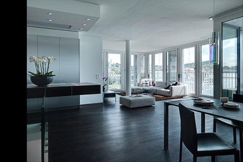 view towards living area with sofas, surrounded by windows, to the right dark table and chair