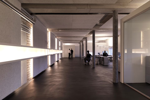 perspective of hallway, office area to the right people sitting and working