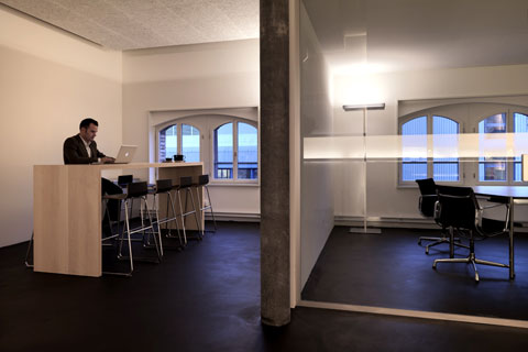 a man sitting on long table working at a laptop, to the right part of conference room